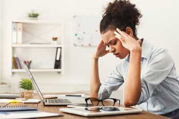 woman-at-desk-rubbing-her-temples-Headache