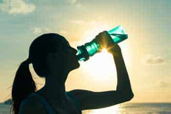 woman-drinks-from-bottle-with-sunrise-in-background